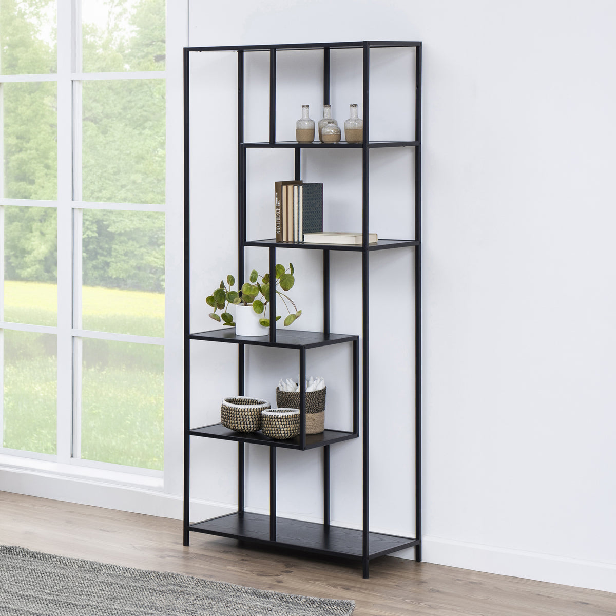 Skeleto bookcase, 77x185, black melamine, by a large window with a plant, baskets and books – a black bookcase for the living room