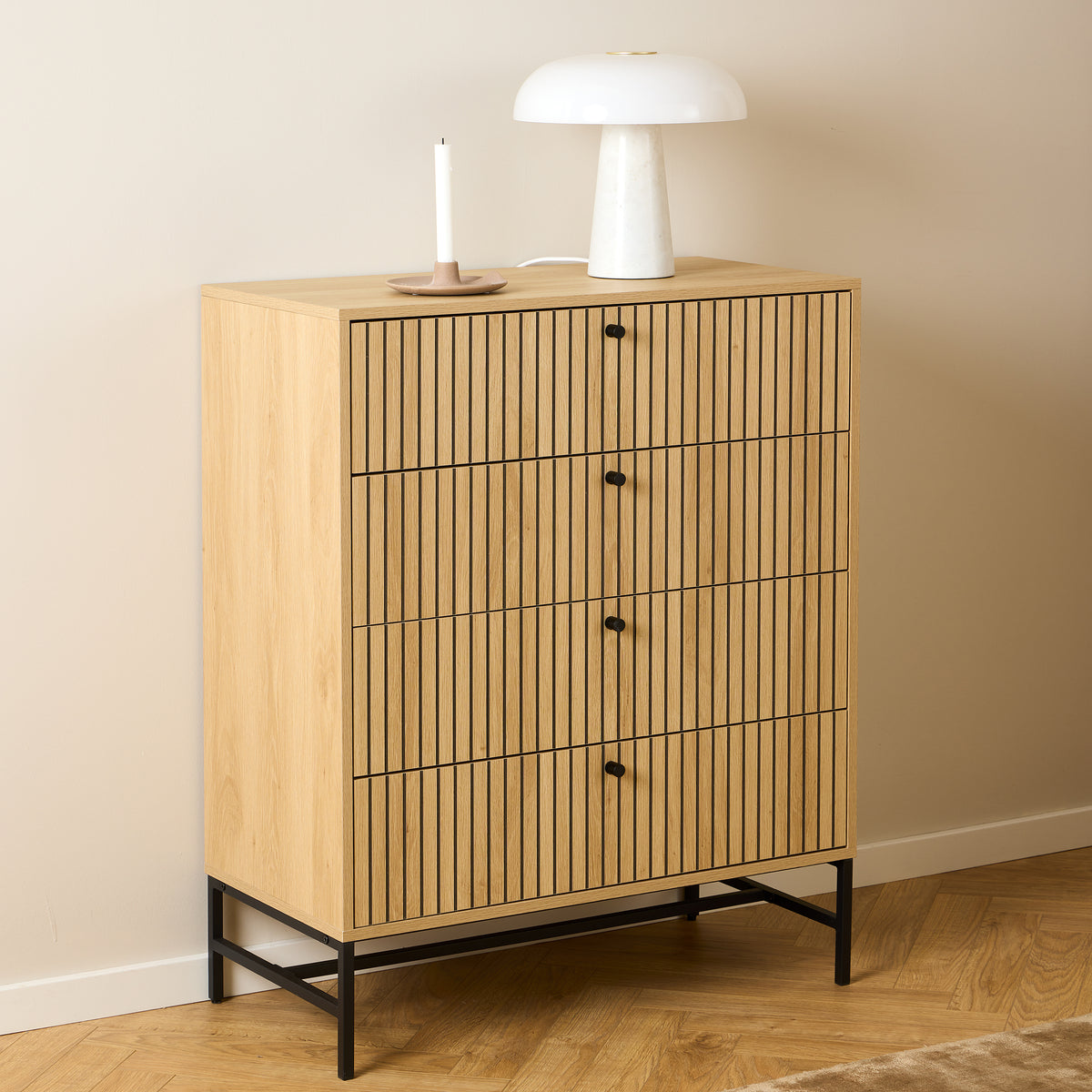 A Bambouz chest of drawers (81x100) against a beige wall, with a white lamp and a candle on a herringbone-patterned parquet floor – a chest of drawers for the bedroom