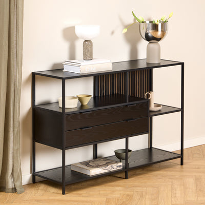 A low Skeleto bookcase (114x78), in black melamine, against a light-coloured wall, with a lamp and a vase of tulips on the top