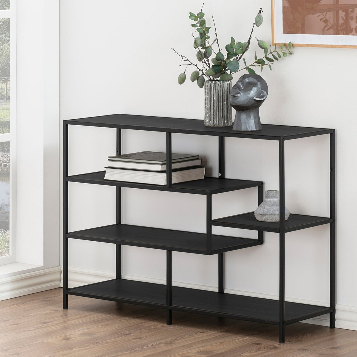 Skeleto bookcase, 114x78, black melamine, by the window with twigs in a vase, a sculpture and books – a black bookcase for the living room