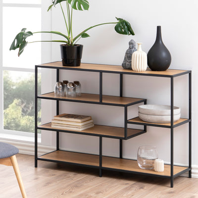 The Skeleto bookcase (114x78), in Wild Oak, in a bright living room by the window, with a plant, vases and books – a bookcase for the living room