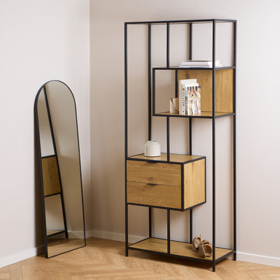 The Skeleto bookcase (77x185), in Wild Oak, in a light-coloured interior next to an arched mirror, with books and a vase on the shelves