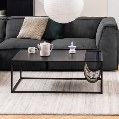 A Skeleto coffee table (110x60) in front of a graphite-coloured sofa on a light-coloured carpet, with a jug and magazines in a metal pocket