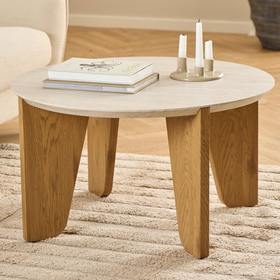 The Tendra coffee table (Ø80x45) on a beige rug next to a light-coloured armchair, with books and a candlestick – a coffee table for the living room