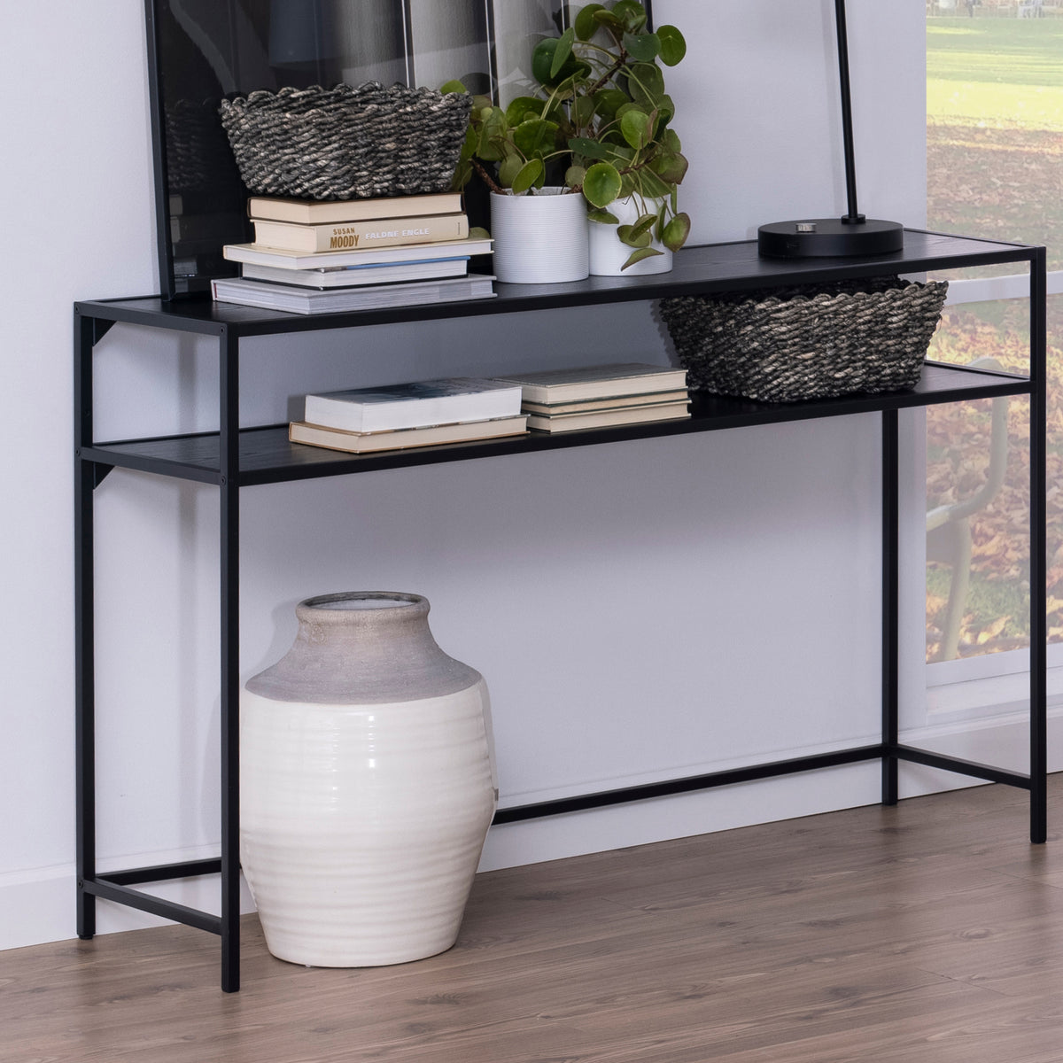 Skeleto console table, 120x79, black melamine, placed against the wall with baskets, books and a plant, with a vase underneath