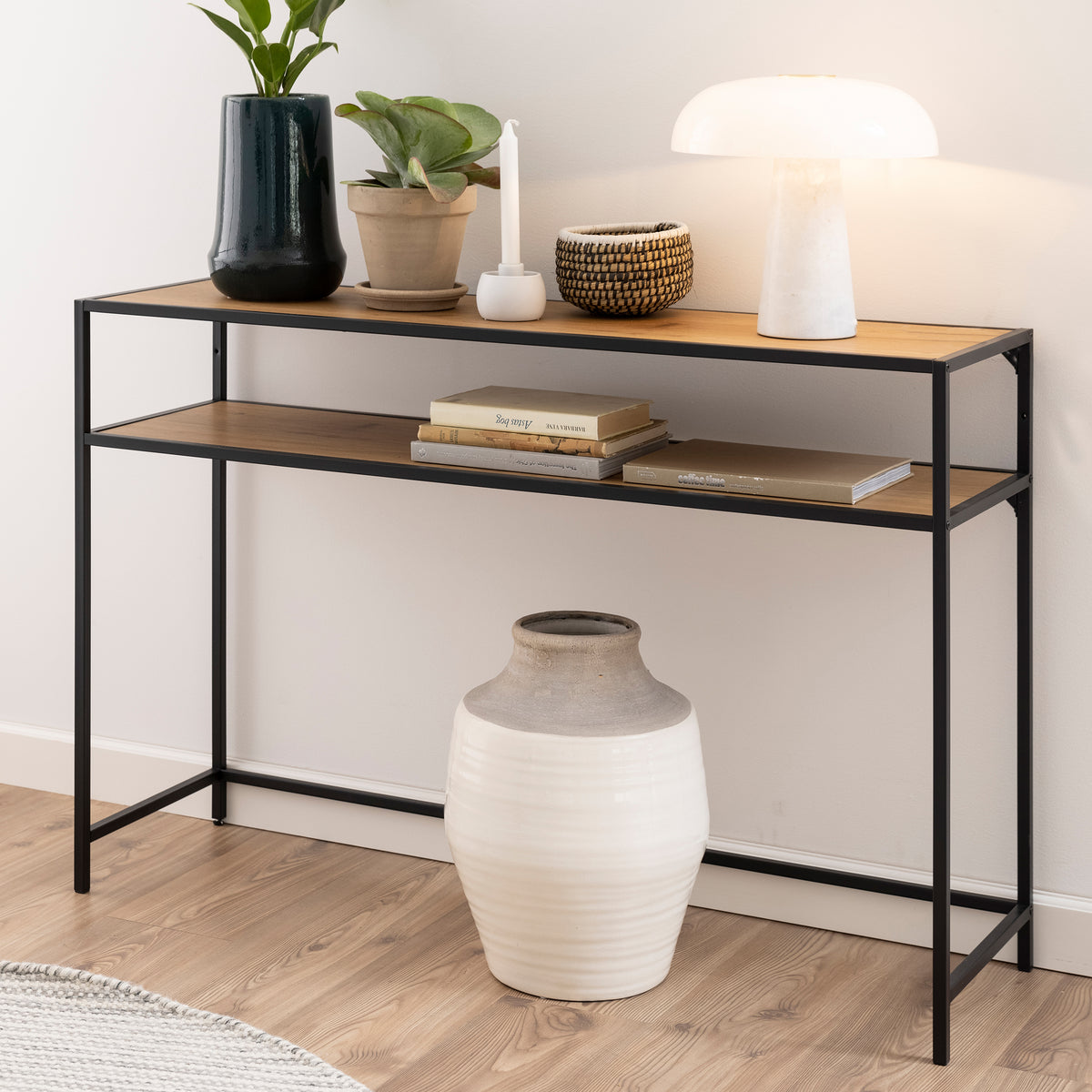 The Skeleto 120x79 Wild Oak console table against a light-coloured wall, with a lamp, plants and books on the shelf – a console table for the hall